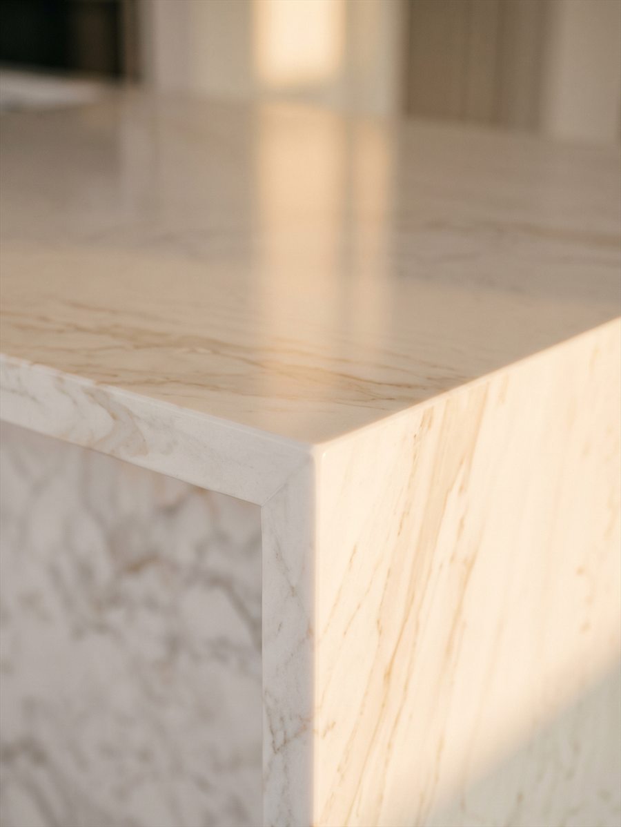 Raking light across a polished white marble kitchen island